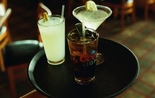 Server carrying a tray of mixed drinks including a margarita, martini, and cola at Terrazza Greenfield