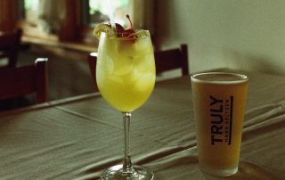 Yellow cocktail garnished with cherry and orange next to a Truly Hard Seltzer at Terrazza Greenfield