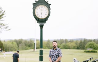 Man standing beside vintage green clock on the golf course grounds at Terrazza Greenfield, with golf carts and green in the background