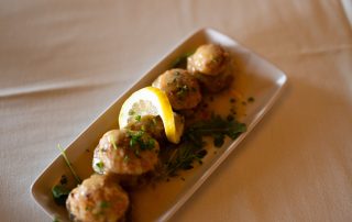Golden crab cakes garnished with lemon and herbs served on a plate at Terrazza Greenfield