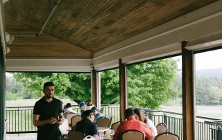 Terrazza Greenfield restaurant server assisting guests dining on the covered outdoor deck with wooded golf course views.